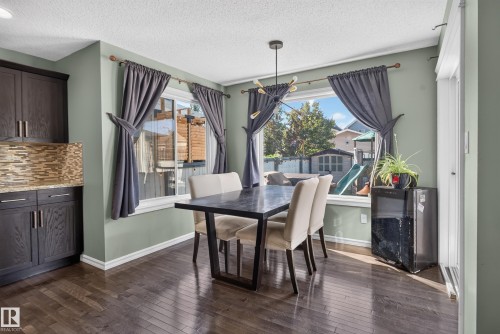 Dark wood-finish flooring, built-in cabinetry with a mosaic tile backsplash, multiple windows, and a contemporary chandelier - 1332 72 Street Sw, Edmonton, AB 