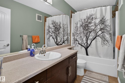 Bathroom featuring a single vanity with an integrated sink, polished chrome faucet, wood-finish cabinetry, and a full-size bathtub - 1332 72 Street Sw, Edmonton, AB 