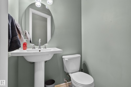 Pedestal sink with chrome fixtures, oval mirror, and wall-mounted lighting - 1332 72 Street Sw, Edmonton, AB 