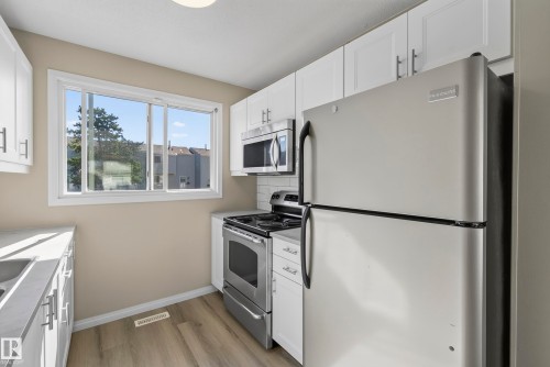 Kitchen featuring white cabinetry, stainless steel appliances, a white subway tile backsplash, and wood-finish flooring - 141 Dickinsfield Court Nw, Edmonton, AB 