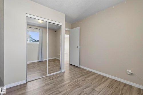 Wood-finish flooring, mirrored sliding closet doors, neutral wall paint, and a bright window with curtain rod - 141 Dickinsfield Court Nw, Edmonton, AB 