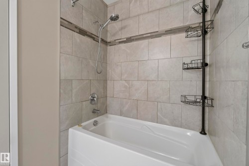 Bathtub with a tiled surround featuring a decorative mosaic accent band and chrome fixtures - 141 Dickinsfield Court Nw, Edmonton, AB 