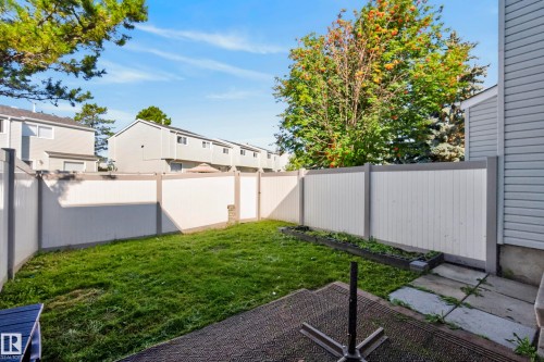 Private fenced yard with a manicured lawn, concrete patio, and garden bed - 141 Dickinsfield Court Nw, Edmonton, AB 