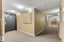 Common area with textured carpet flooring, cream-painted walls, and ceiling-mounted lighting fixtures - #208 18122 77 St Nw, Edmonton, AB 
