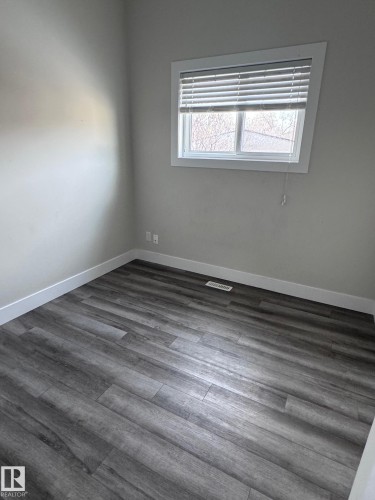 Spacious room featuring wood-finish flooring, light grey wall paint, and white baseboards - 7604 7606 75 Street Nw, Edmonton, AB - Indoor Photo Showing Other Room