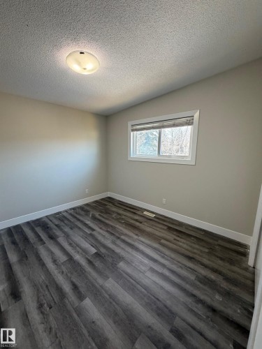 Spacious room featuring wood-finish flooring, neutral-toned walls, and a large window providing natural light - 7604 7606 75 Street Nw, Edmonton, AB - Indoor Photo Showing Other Room