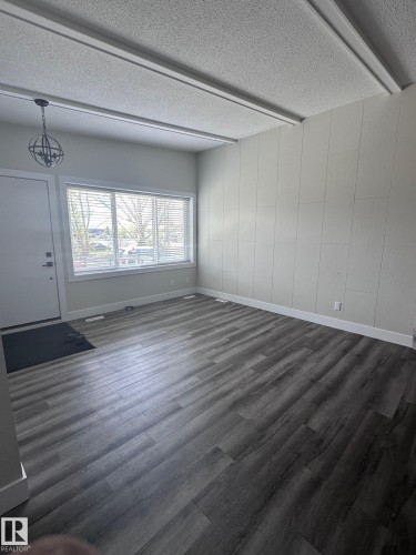 Spacious room featuring wood-finish flooring, a contemporary black orb chandelier, and large windows with blinds - 7604 7606 75 Street Nw, Edmonton, AB - Indoor Photo Showing Other Room