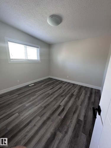 Spacious room featuring wood-finish flooring, white baseboards, and a neutral wall palette - 7604 7606 75 Street Nw, Edmonton, AB - Indoor Photo Showing Other Room