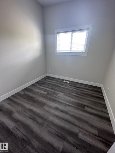 Spacious room featuring dark wood-finish flooring, light grey walls, white trim, a single window with blinds, and a floor vent - 7604 7606 75 Street Nw, Edmonton, AB - Indoor Photo Showing Other Room
