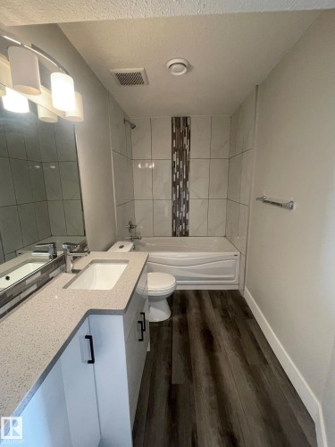 Bathroom featuring a white vanity with an integrated sink, a light-colored countertop, and a full-width mirror - 7604 7606 75 Street Nw, Edmonton, AB - Indoor Photo Showing Bathroom