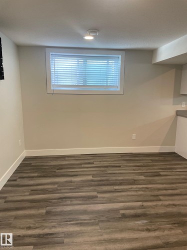 Spacious room featuring wood-finish flooring, neutral paint, a window with blinds, recessed lighting, and white baseboards - 7604 7606 75 Street Nw, Edmonton, AB - Indoor