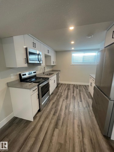 Modern kitchen featuring light wood-finish flooring, white cabinetry with dark hardware, stainless steel appliances, and recessed lighting - 7604 7606 75 Street Nw, Edmonton, AB - Indoor Photo Showing Kitchen