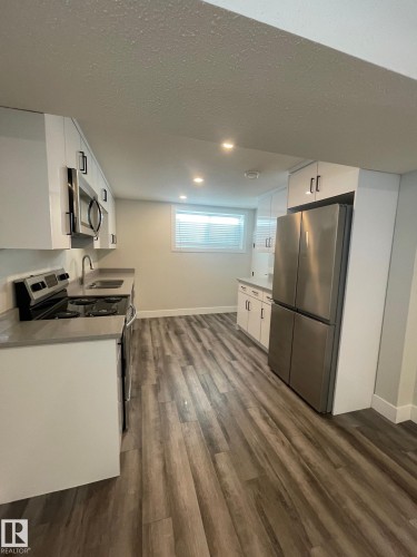 Contemporary kitchen featuring white cabinetry with black hardware, stainless steel appliances, light-toned countertops, wood-finish flooring, and recessed lighting - 7604 7606 75 Street Nw, Edmonton, AB - Indoor Photo Showing Kitchen