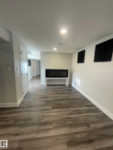 Spacious interior room featuring wood-finish flooring, a built-in electric fireplace with a white mantel, recessed lighting, and crisp white trim - 7604 7606 75 Street Nw, Edmonton, AB - Indoor With Fireplace