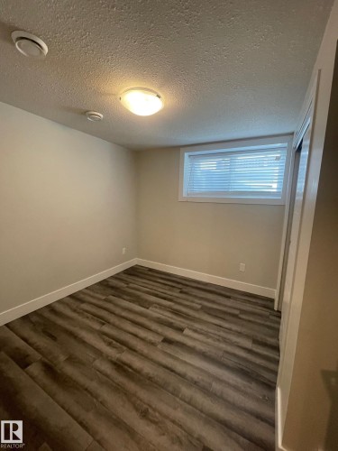 Room featuring wood-finish flooring, a white window frame with blinds, and neutral painted walls - 7604 7606 75 Street Nw, Edmonton, AB - Indoor