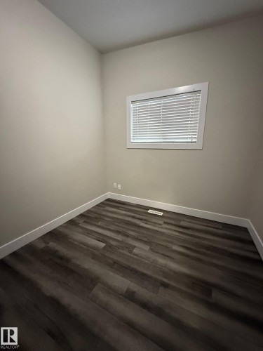 Room featuring wood-finish flooring, neutral wall paint, white baseboards, and a window with blinds - 7604 7606 75 Street Nw, Edmonton, AB - Indoor Photo Showing Other Room