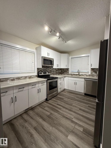 Modern kitchen featuring white cabinetry, light-toned countertops, a full suite of stainless steel appliances, and wood-finish flooring - 7604 7606 75 Street Nw, Edmonton, AB - Indoor Photo Showing Kitchen