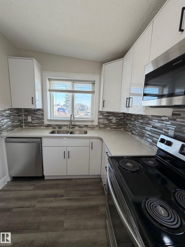 Kitchen featuring sleek white cabinetry, light-toned countertops, a mosaic tile backsplash, stainless steel appliances, and wood-finish flooring - 7604 7606 75 Street Nw, Edmonton, AB - Indoor Photo Showing Kitchen With Double Sink