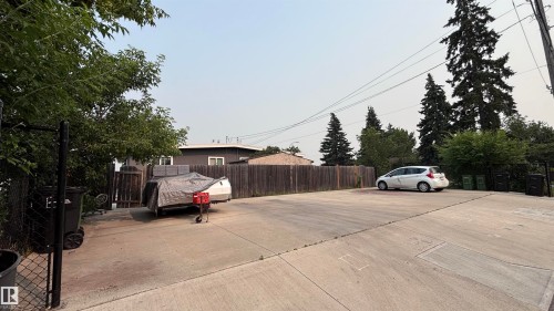 Concrete parking pad framed by a wood privacy fence and mature trees - 7604 7606 75 Street Nw, Edmonton, AB - Outdoor