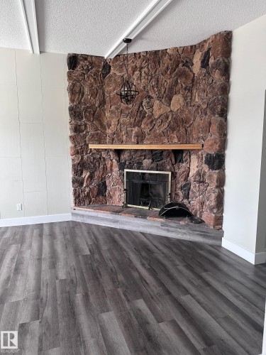 Stone-clad fireplace with a wood mantel and black metal firebox - 7604 7606 75 Street Nw, Edmonton, AB - Indoor Photo Showing Living Room With Fireplace