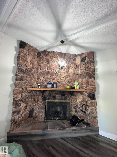 Corner fireplace featuring a stone surround, a wood mantel, and a stone hearth with wood-finish flooring - 7604 7606 75 Street Nw, Edmonton, AB - Indoor With Fireplace