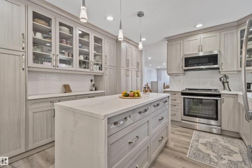 Kitchen featuring a central island with a light-toned countertop, extensive cabinetry with glass-front uppers, stainless steel appliances, and wood-finish flooring - 18812 89 Avenue Nw, Edmonton, AB 