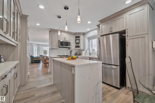 Kitchen featuring light wood-finish cabinetry, stainless steel appliances, a center island with a waterfall countertop, and wood-finish flooring - 18812 89 Avenue Nw, Edmonton, AB 