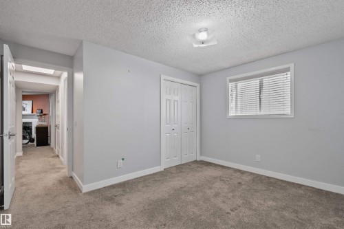 Recessed window with blinds, white trim throughout, textured ceiling, bi-fold closet doors, and neutral carpet flooring - 18812 89 Avenue Nw, Edmonton, AB 