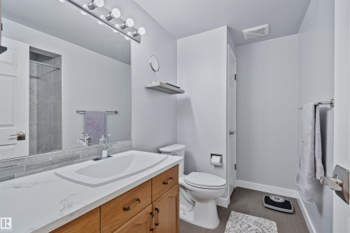 Vanity with a white countertop and integrated sink, wood-finish cabinetry, chrome faucet, and subway tile backsplash - 18812 89 Avenue Nw, Edmonton, AB 