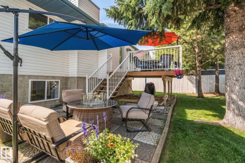 Tiered outdoor living space featuring a wooden deck with white railings, a lower patio with patterned pavers, and a manicured lawn - 18812 89 Avenue Nw, Edmonton, AB 