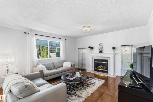 Hardwood flooring, crown molding, a fireplace with a stone surround, a white mantel, and a recessed firebox - 522 Klarvatten Lake Wynd Nw, Edmonton, AB 