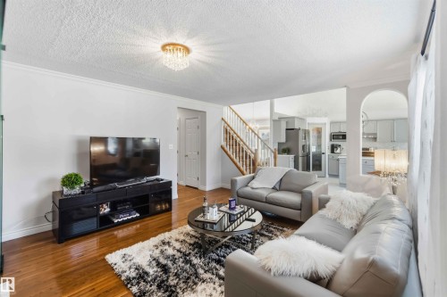 Hardwood flooring, crystal flush mount lighting, painted wood staircase with wood handrail, arched doorway, and crown molding - 522 Klarvatten Lake Wynd Nw, Edmonton, AB 