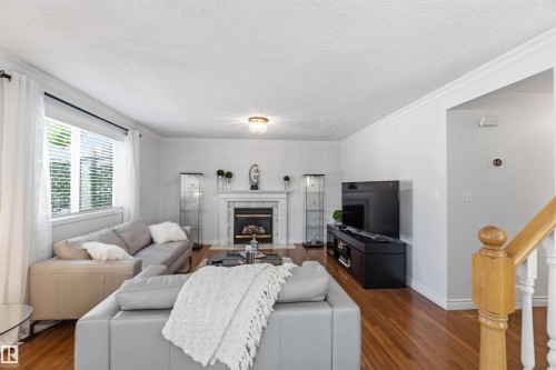 Living area featuring wood-finish flooring, a fireplace with a stone surround, crown molding, and a chandelier - 522 Klarvatten Lake Wynd Nw, Edmonton, AB 