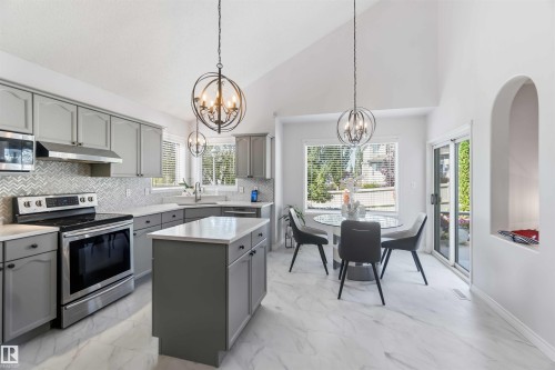 Kitchen featuring gray cabinetry, stainless steel appliances, a chevron-patterned backsplash, and light-toned stone countertops - 522 Klarvatten Lake Wynd Nw, Edmonton, AB 