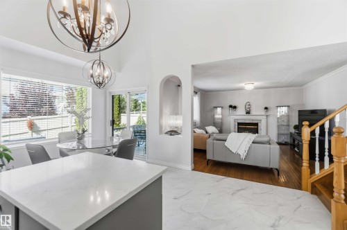 Vaulted ceiling with decorative chandeliers, bay window, sliding glass door, fireplace with mantel, and wood-finish flooring - 522 Klarvatten Lake Wynd Nw, Edmonton, AB 