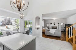 Vaulted ceiling with decorative chandeliers, bay window, sliding glass door, fireplace with mantel, and wood-finish flooring - 