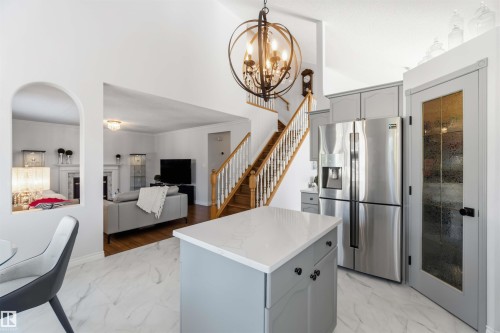 Vaulted ceilings with an orb chandelier, wood staircase with white balusters, stainless steel French door refrigerator, light gray cabinetry, and a pantry with a textured glass door - 522 Klarvatten Lake Wynd Nw, Edmonton, AB 