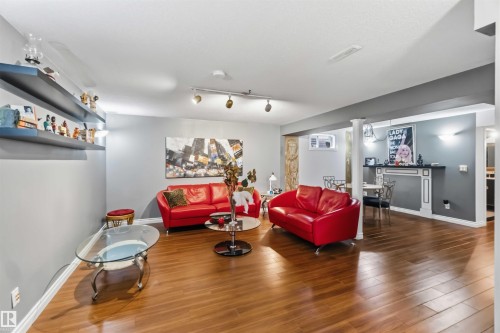 Spacious room featuring wood-finish flooring, track lighting, built-in shelving, decorative wall sconces, and a decorative fireplace - 522 Klarvatten Lake Wynd Nw, Edmonton, AB 