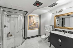 Three-piece bathroom featuring a curved glass shower enclosure, white tile flooring, a dark wood vanity with a white countertop, and a gold-framed mirror - 
