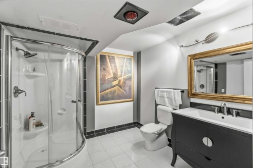 Three-piece bathroom featuring a curved glass shower enclosure, white tile flooring, a dark wood vanity with a white countertop, and a gold-framed mirror - 522 Klarvatten Lake Wynd Nw, Edmonton, AB 