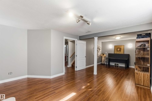 Wood-finish flooring throughout, track lighting, ceiling-mounted light fixture, recessed wall sconces, and built-in wood shelving with glass doors - 522 Klarvatten Lake Wynd Nw, Edmonton, AB 
