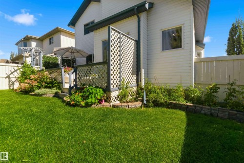 Expansive lawn with a tiered garden bed featuring mature shrubs and plantings, wood privacy fencing, and a raised exterior deck with lattice details - 522 Klarvatten Lake Wynd Nw, Edmonton, AB 