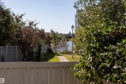 White picket fence with a paved pathway, mature trees, and a distant body of water - 
