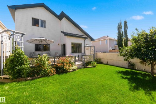 Expansive green lawn with mature trees, a multi-level deck featuring lattice railing, and a side yard arbor - 522 Klarvatten Lake Wynd Nw, Edmonton, AB 