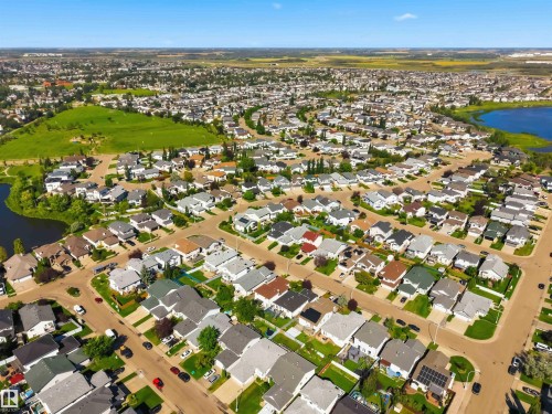 Residential neighborhood featuring a consistent architectural style, mature landscaping, paved streets, and a nearby open green space - 522 Klarvatten Lake Wynd Nw, Edmonton, AB 