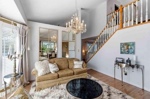 Two-story foyer with wood-finish flooring, a grand staircase featuring white spindles and wood handrails, and a crystal chandelier - 522 Klarvatten Lake Wynd Nw, Edmonton, AB 