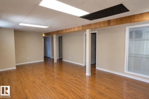 Spacious room featuring wood-finish flooring, neutral-toned walls, and recessed fluorescent lighting - 10439 36A Ave Nw, Edmonton, AB 