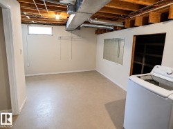Unfinished basement with exposed wood joists and ductwork, featuring neutral painted walls, a horizontal window, and wire shelving - 