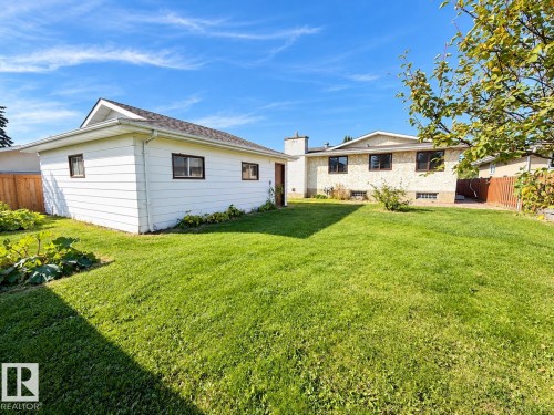 Expansive green lawn, detached white siding garage, brown trim windows, and a wood fence - 10439 36A Ave Nw, Edmonton, AB 