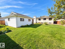 Expansive green lawn, detached white siding garage, brown trim windows, and a wood fence - 